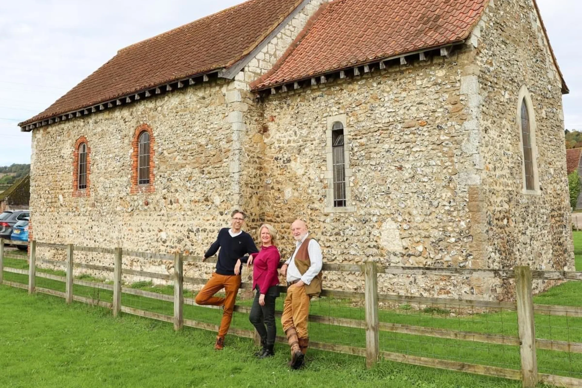Three friends of St. Benedict's, Paddlesworth leaning against the fence outside the church, posing for a picture