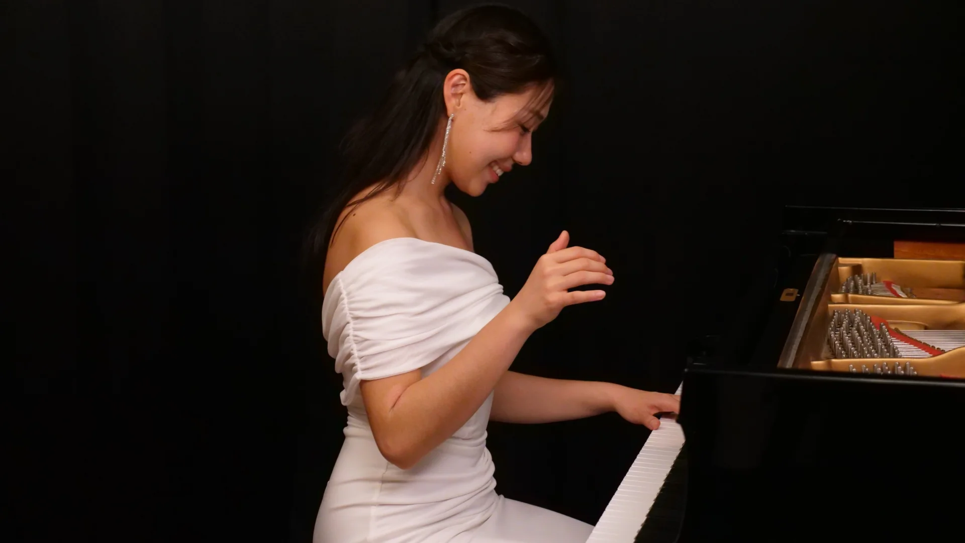 lady with long black hair in a white dress playing a grand piano on a black background