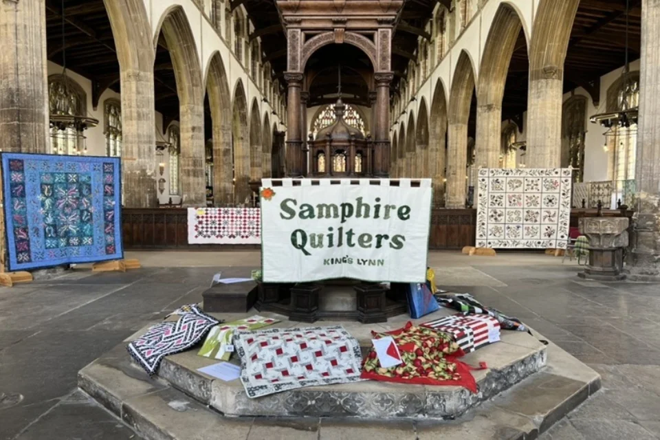 The font at St Nicholas' Chapel Kings Lynn with patchwork quilts placed around, one hanging saying Samphire Quilters