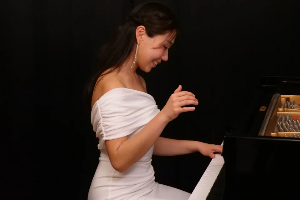 lady with long black hair in a white dress playing a grand piano on a black background