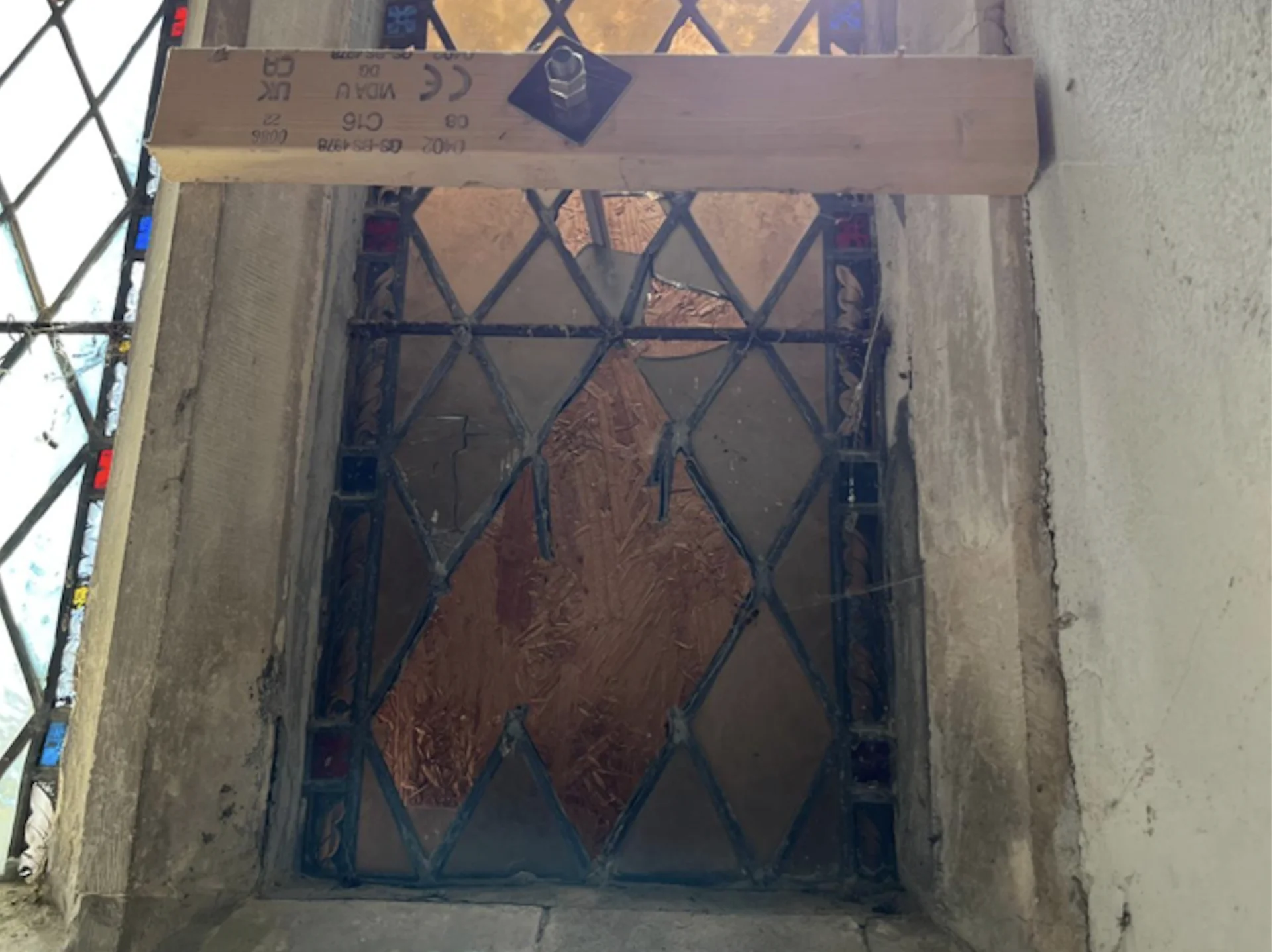 A broken diamond leaded window set in a deep stone surround. Wood has been added to keep it stable.