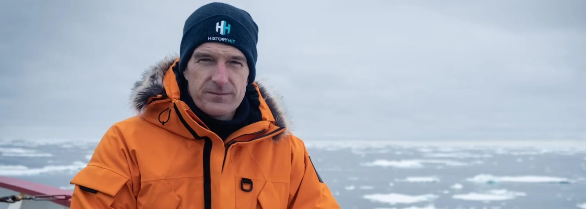 Historian wearing outdoor gear on a boat surrounded by icebergs