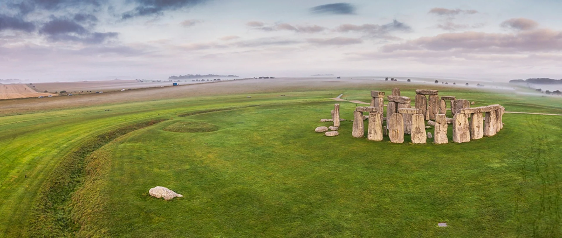 Panoramic wideshot with stone circle on right on grass with to the left fields in background
