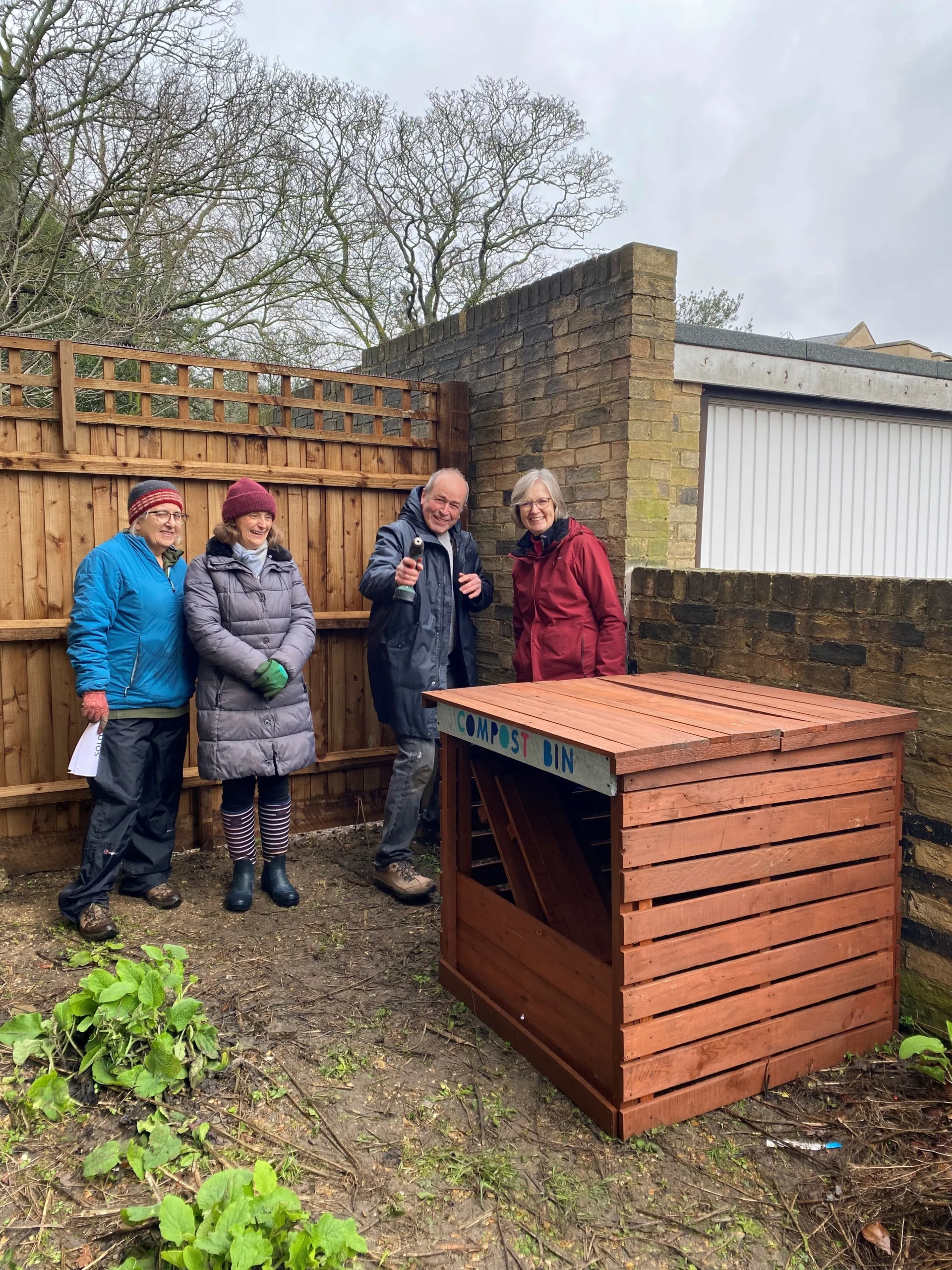 Four volunteers posing outside with a compost bin
