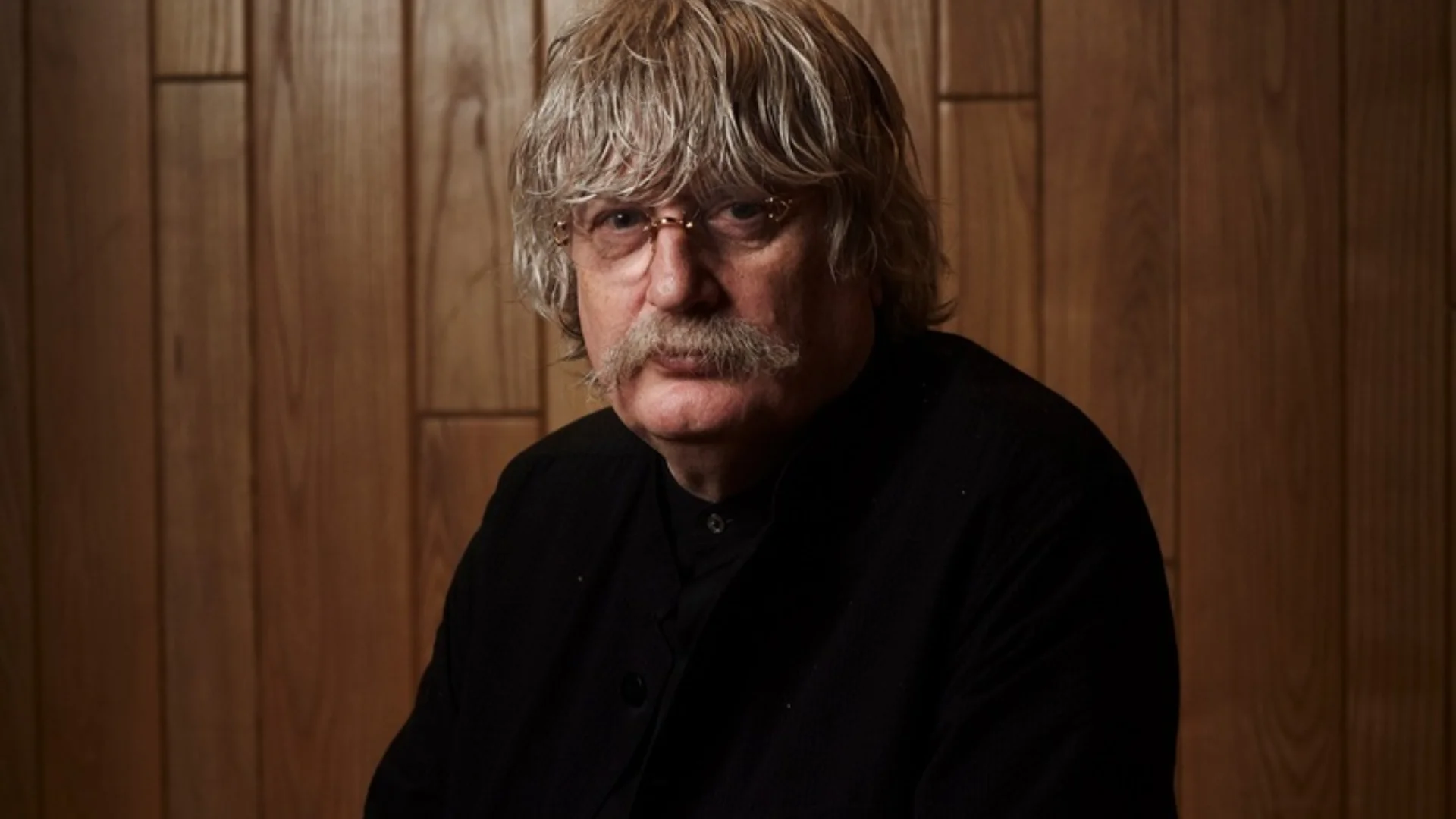 gentleman with medium length hair, moustache, wearing rimless glasses and a black top