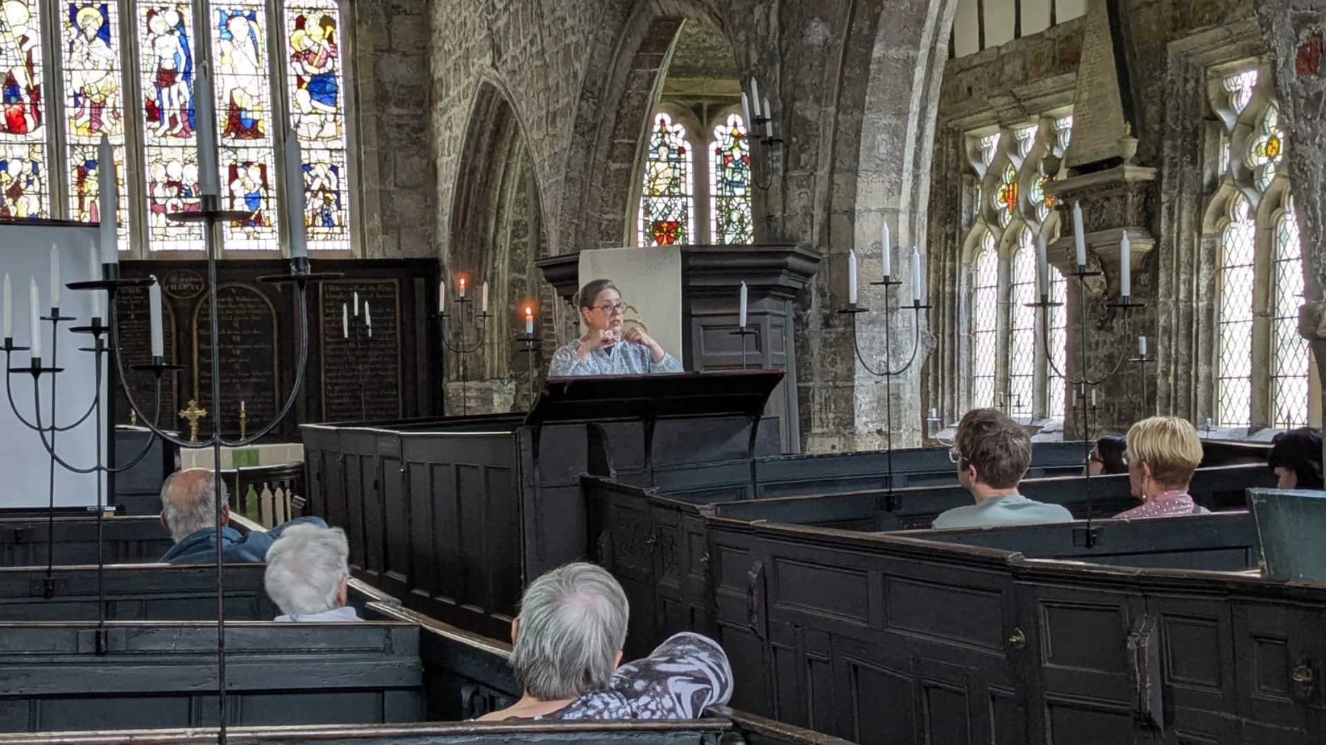 Pat speaking from the pulpit with stained glass windows in background