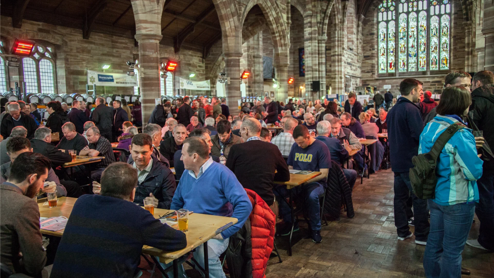Church nave filled with people at tables. Kegs of beer visible in background.