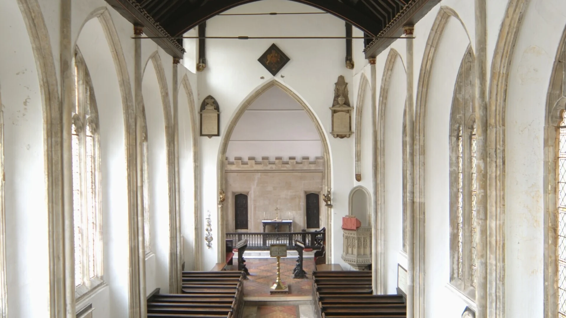 A view of a church looking towards the altar from the gallery, with medieval columns and dark wood Victorian pews