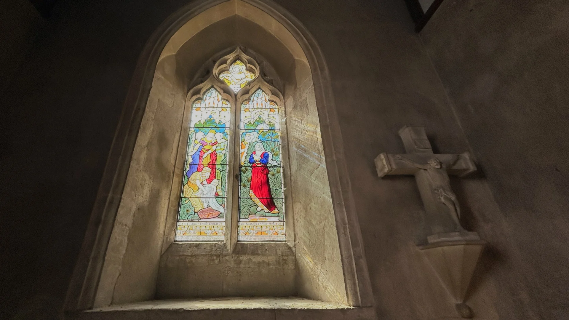 Stained glass window with a stone cross mounted to the right hand side