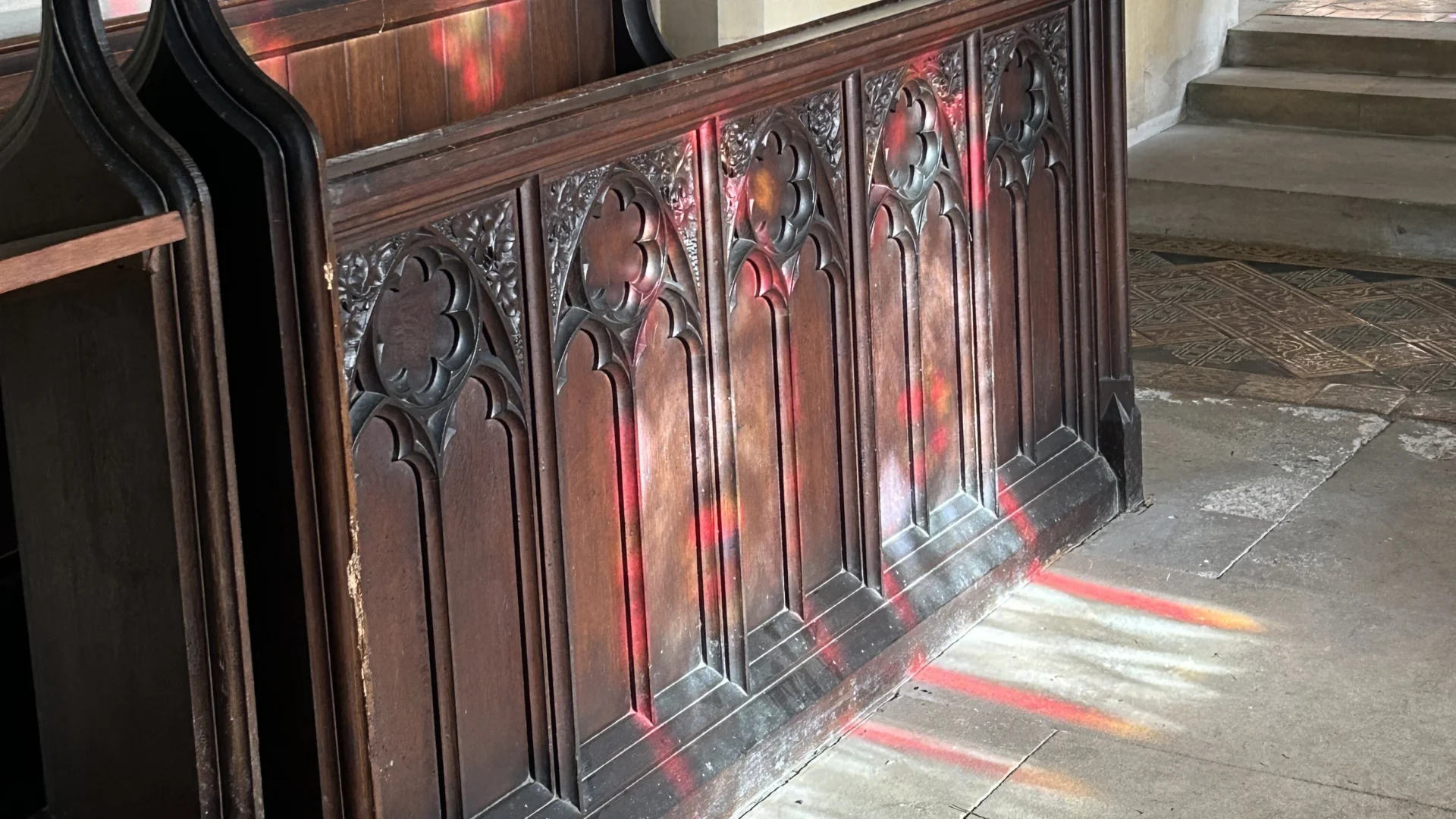 Red and purple stained glass windows reflected across the choir pew and floor of the church