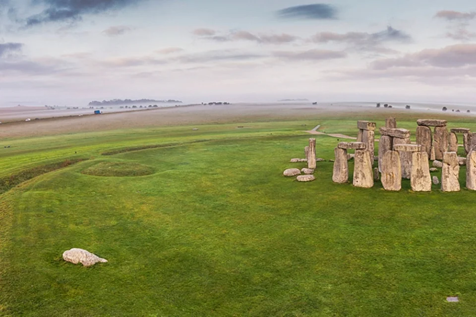 Panoramic wideshot with stone circle on right on grass with to the left fields in background