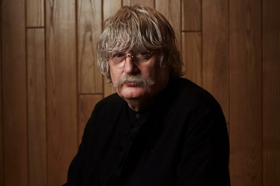 gentleman with medium length hair, moustache, wearing rimless glasses and a black top