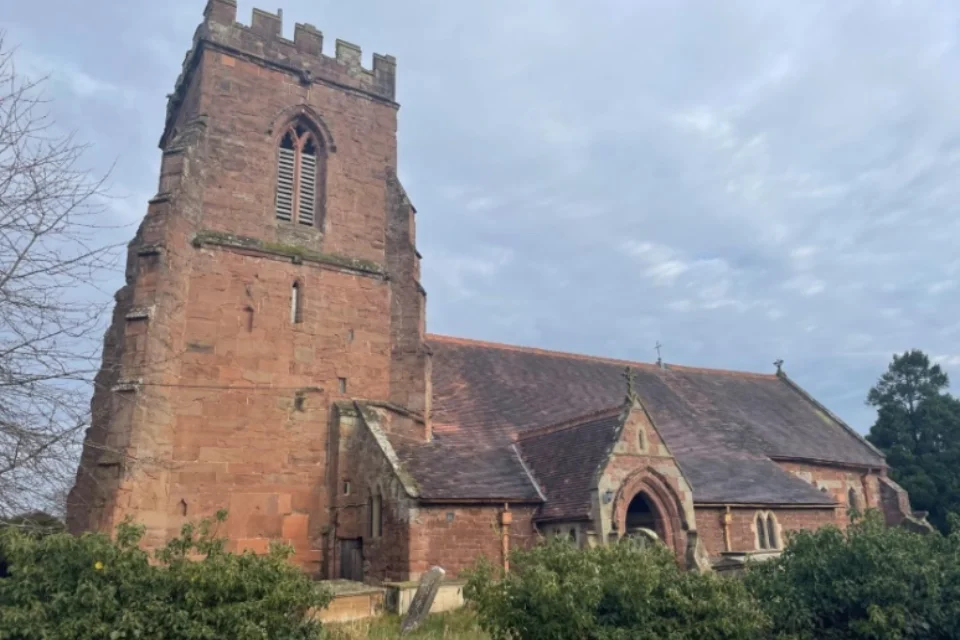 A sandstone church with a square tower in a churchyard with greenery surrounding it.