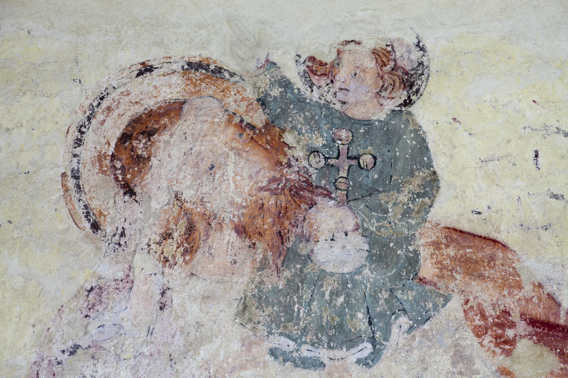 A wall painting detail of St. Christopher - here depicted as a giant man with blue eyes, red hair and a red beard - carrying the Christ child on his shoulder. The Christ child has red hair and a green-bluish dress. He blesses St. Christopher with one hand, while holding a globus cruciger - a ball with a cross on top, representing his sovereignty over the whole world - in the other.